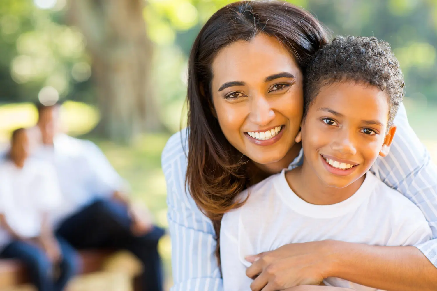 A young woman with long brown hair smiles warmly at the camera in front of a leafy green bush on a sunny day, reflecting the friendly atmosphere of Pediatric Dentistry and Orthodontics of Forsyth - Cumming in Cumming, GA.