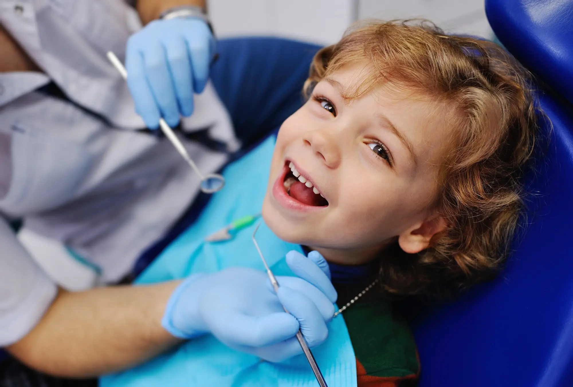 At Pediatric Dentistry and Orthodontics of Forsyth - Cumming in Cumming, GA, a young boy sits in a dental chair with a blue bib while the dentist explains the Preventive Pediatric Dental Care Checkup Schedule by age.