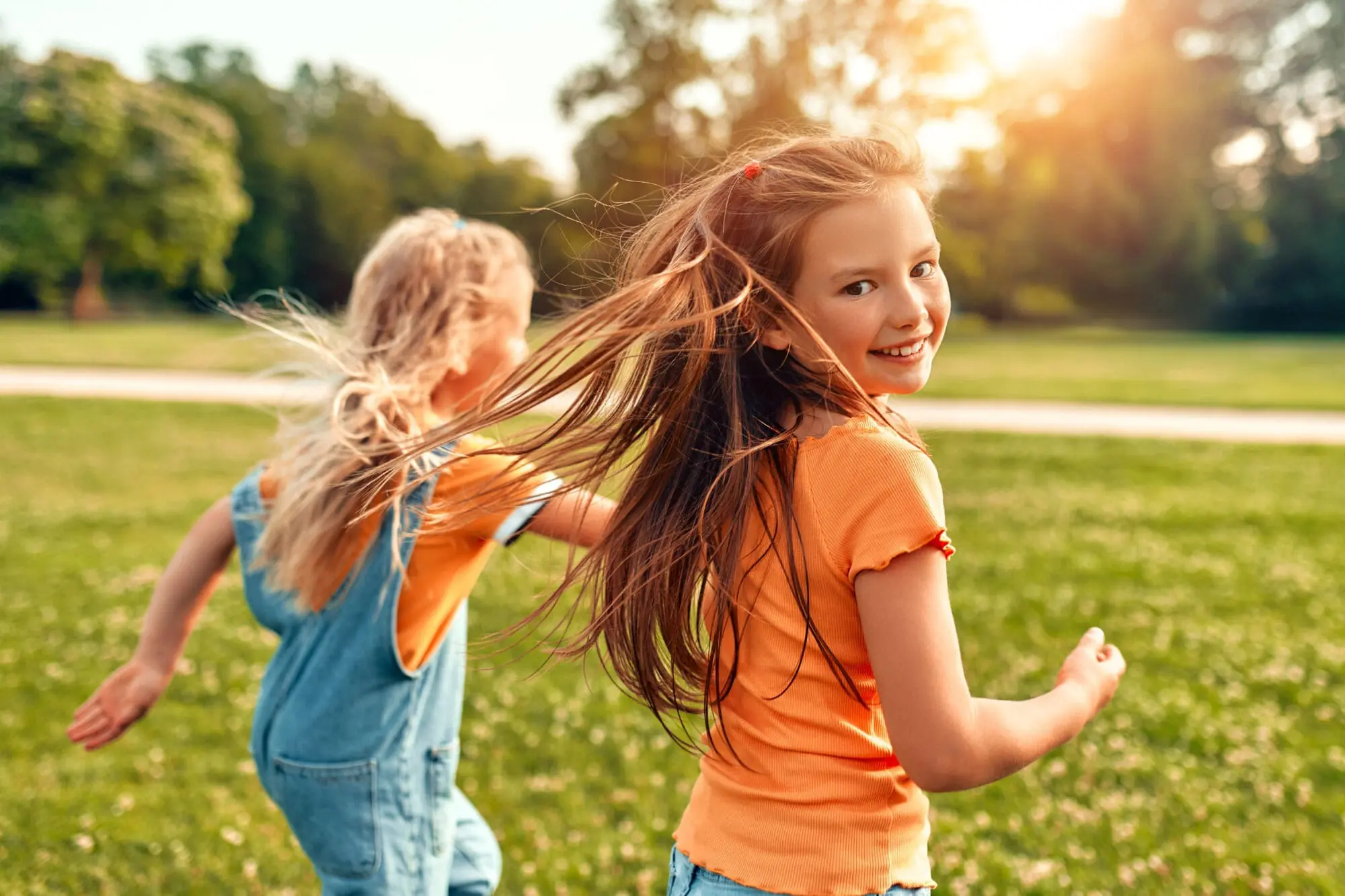 Two young girls play in outdoors, demonstrate the comfort and confidence children experience from pain-free laser dental restoration—one looking thoughtful and the other smiling energetically at Pediatric Dentistry and Orthodontics of Forsyth - Cumming in Cumming, GA.
