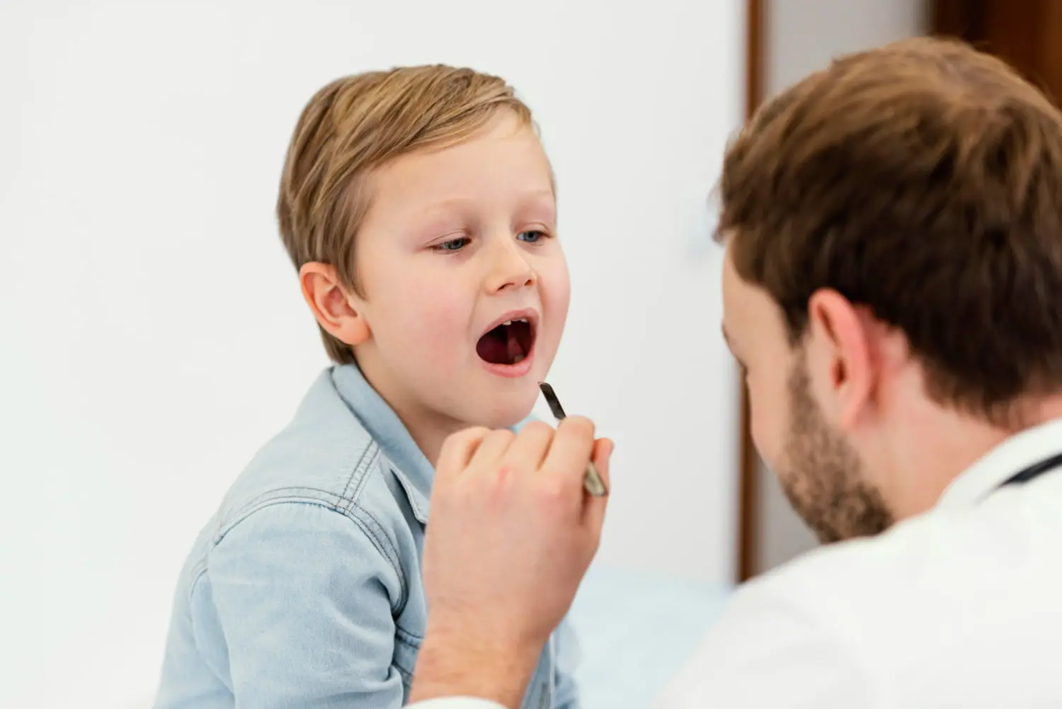 At Pediatric Dentistry and Orthodontics of Forsyth - Cumming in Cumming, GA. A young boy sits in the dental chair with a pediatist during examines her Frenectomies & Canker Sores care appointment.