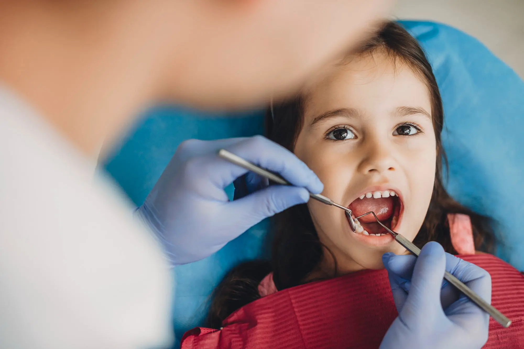 At Pediatric Dentistry and Orthodontics of Forsyth - Cumming in Cumming GA. A dentist wearing black gloves examines a young child's teeth, emphasizing the importance of early orthodontics and partnering with local orthodontists to ensure healthy smiles.
