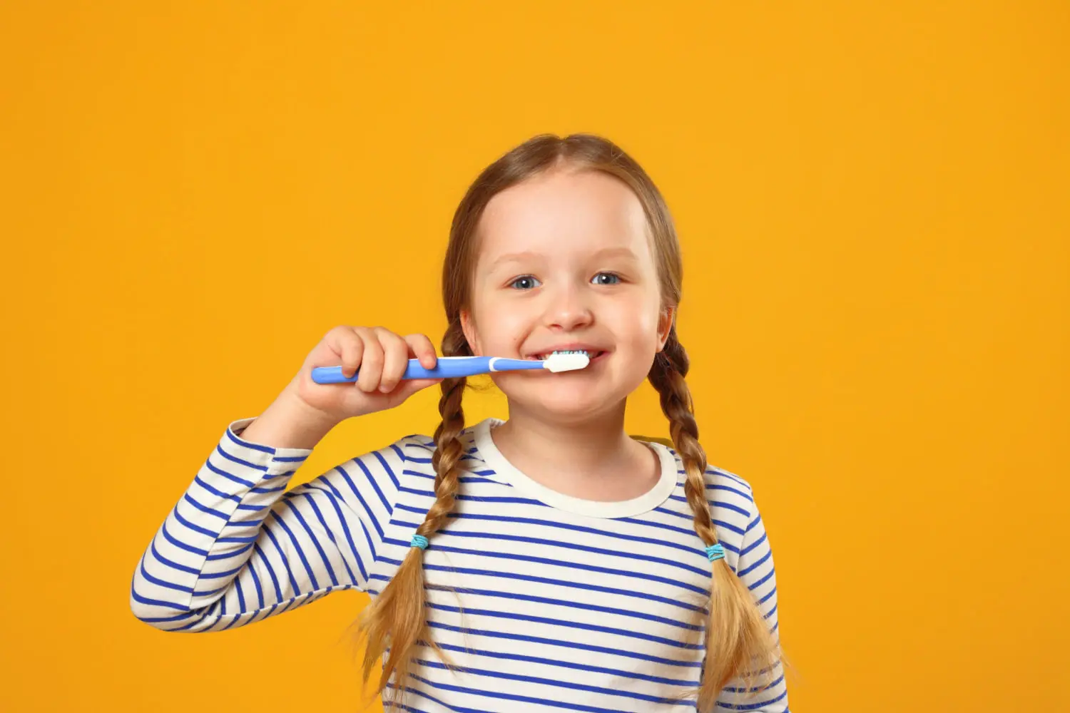 A smiling young girl brushes their teeth in a brightly lit room, highlighting good oral health and restorative dentistry at Pediatric Dentistry and Orthodontics of Forsyth - Cumming in Cumming, GA.