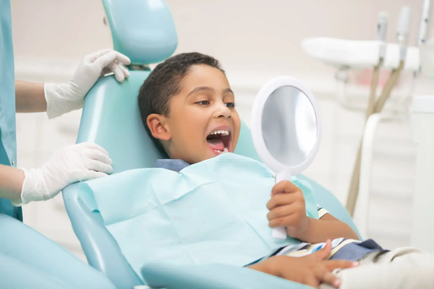 At Pediatric Dentistry and Orthodontics of Forsyth - Cumming in Cumming GA, a young child sits in the dental chair, happily using a square mirror to check their teeth and identify potential tongue or lip ties.