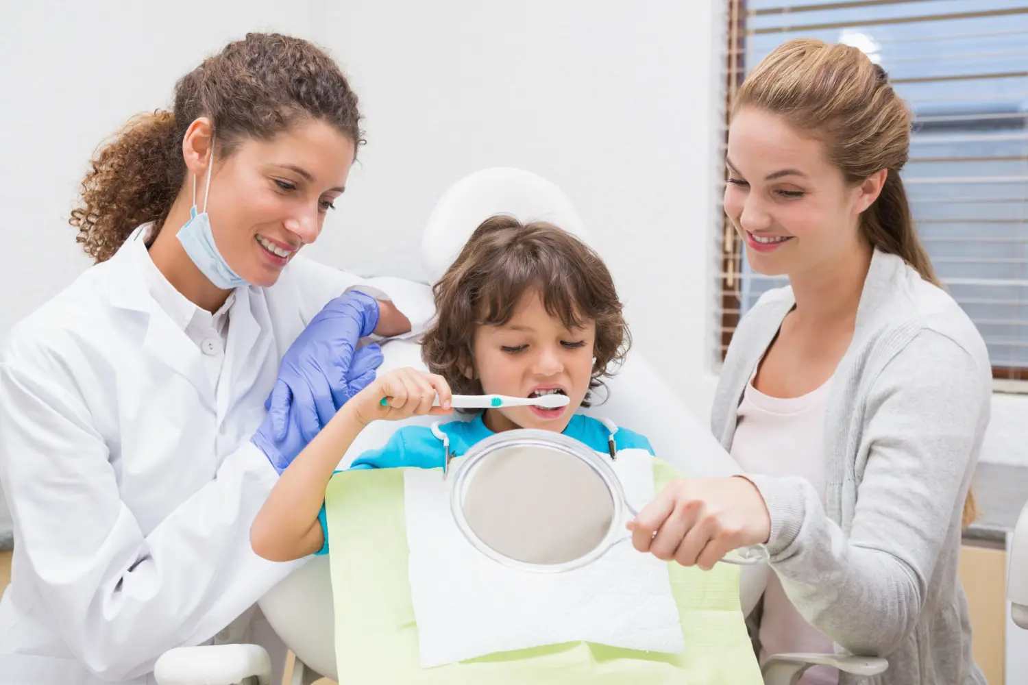 At Pediatric Dentistry and Orthodontics of Forsyth - Cumming in Cumming, GA, a dentist demonstrates proper brushing techniques to a young boy using a dental model, emphasizing the significance of preventive pediatric dental care. Preventive services for children are covered by Apple Health.
