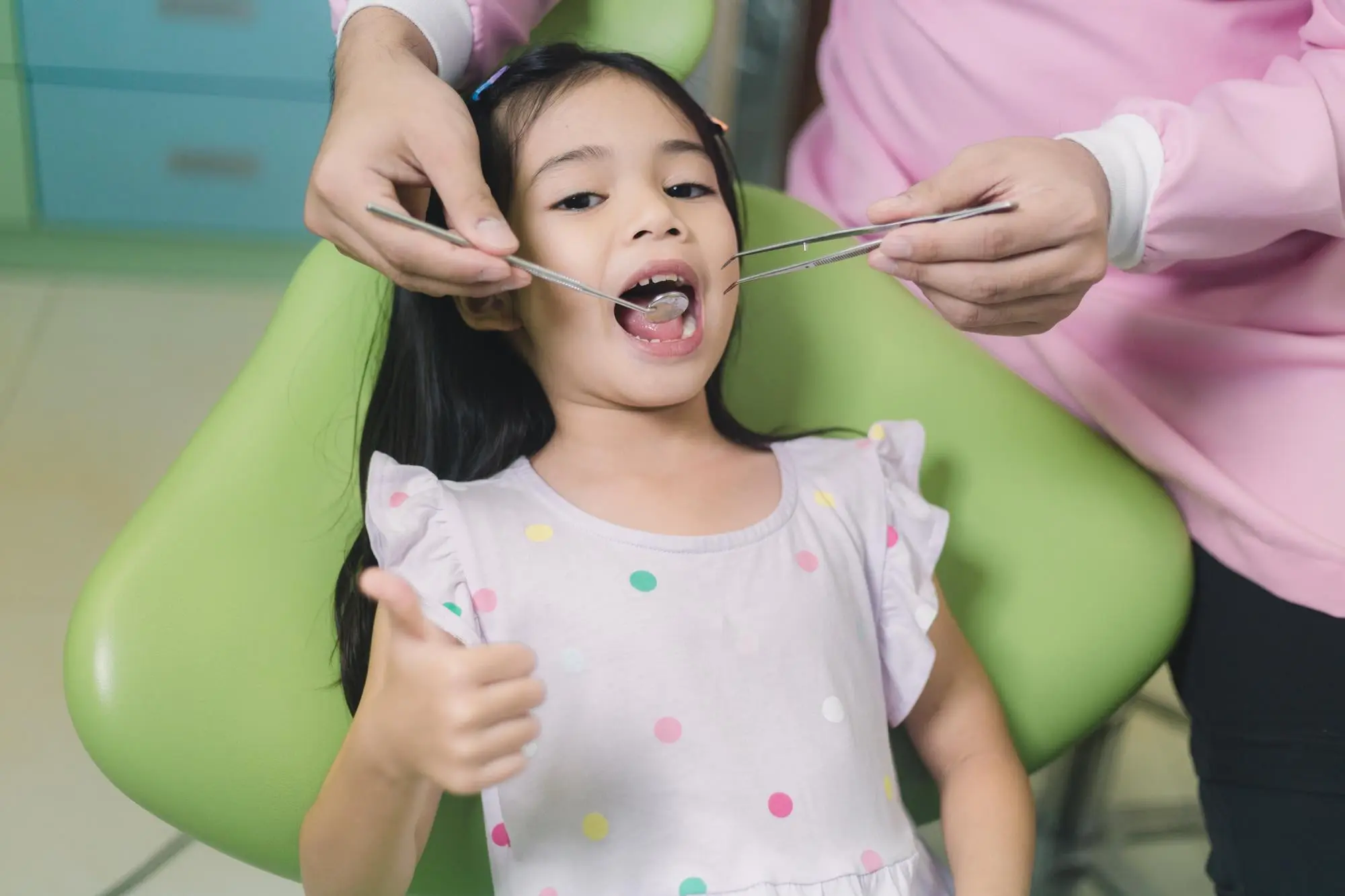 A young child smiles in the dental chair as the dentist gently holds instruments nearby, demonstrating the advantages of a sensory-Friendly Dentist office in Cumming, GA.