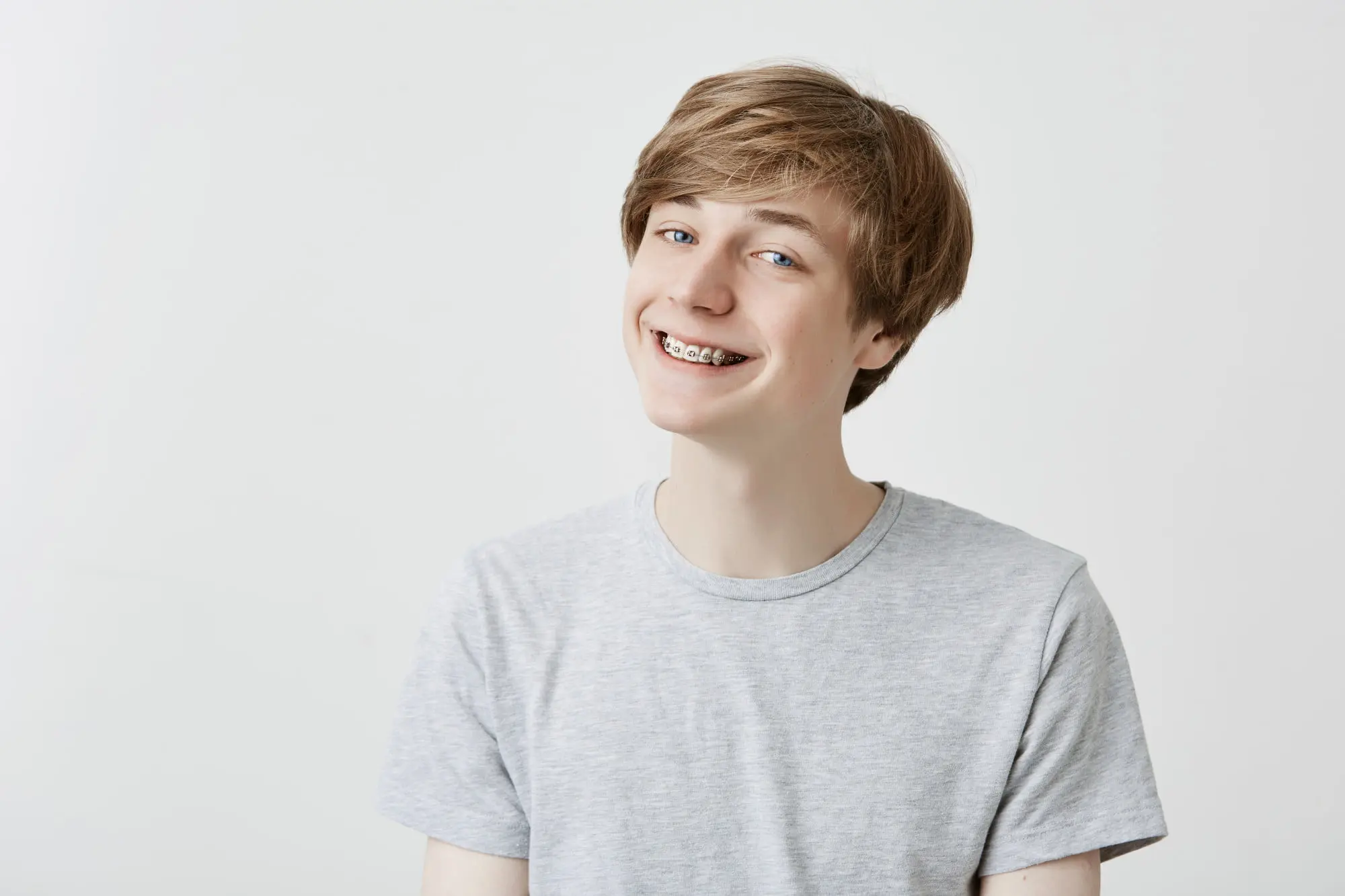 Smiling teen boy with light brown hair, grey t-shirt, and braces at Pediatric Dentistry and Orthodontics of Forsyth - Cumming in Cumming, GA.