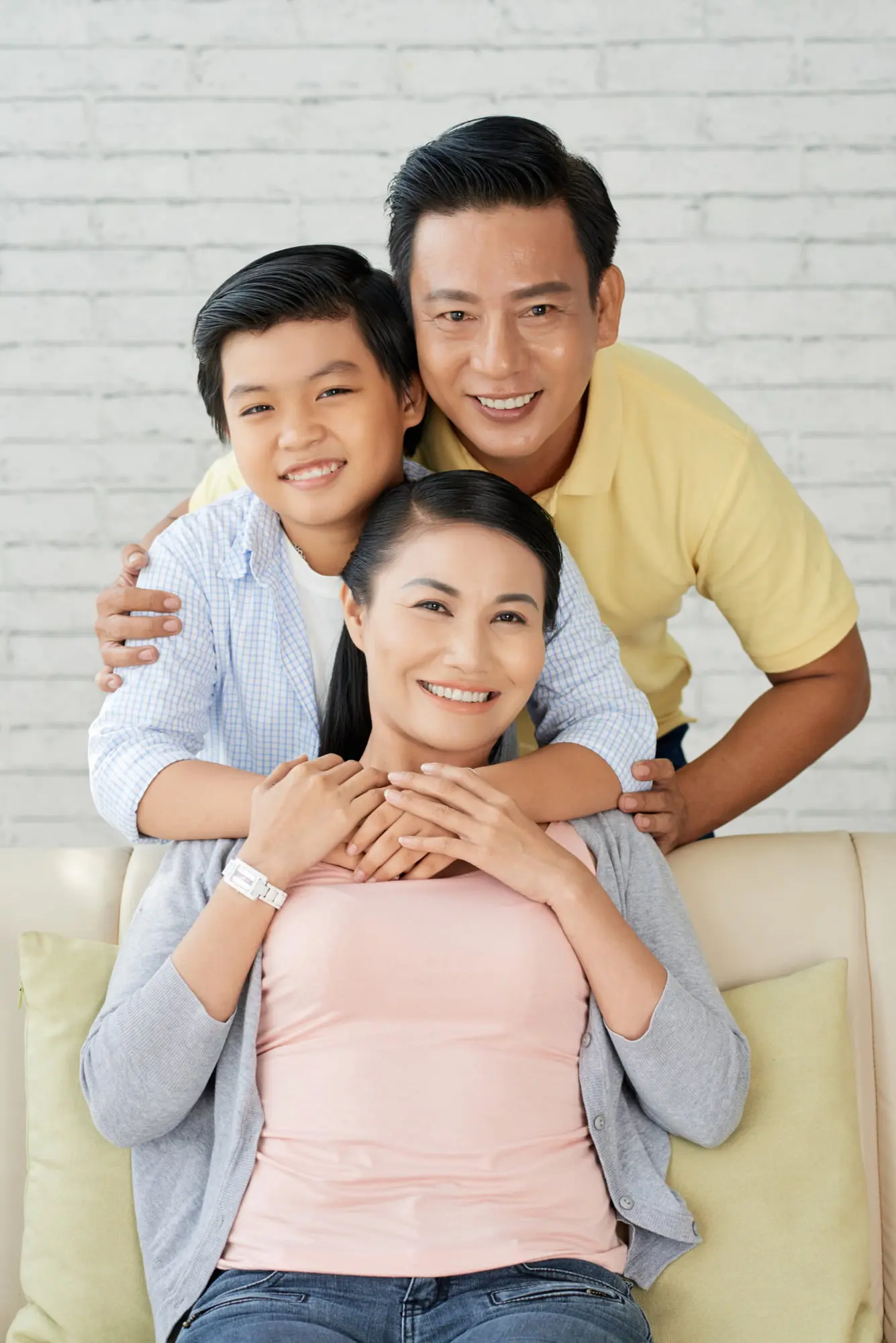 Smiling family poses indoors at Forsyth Pediatric Dentistry and Orthodontics in Cumming, GA: woman on couch, man and child behind after overbite treatment.