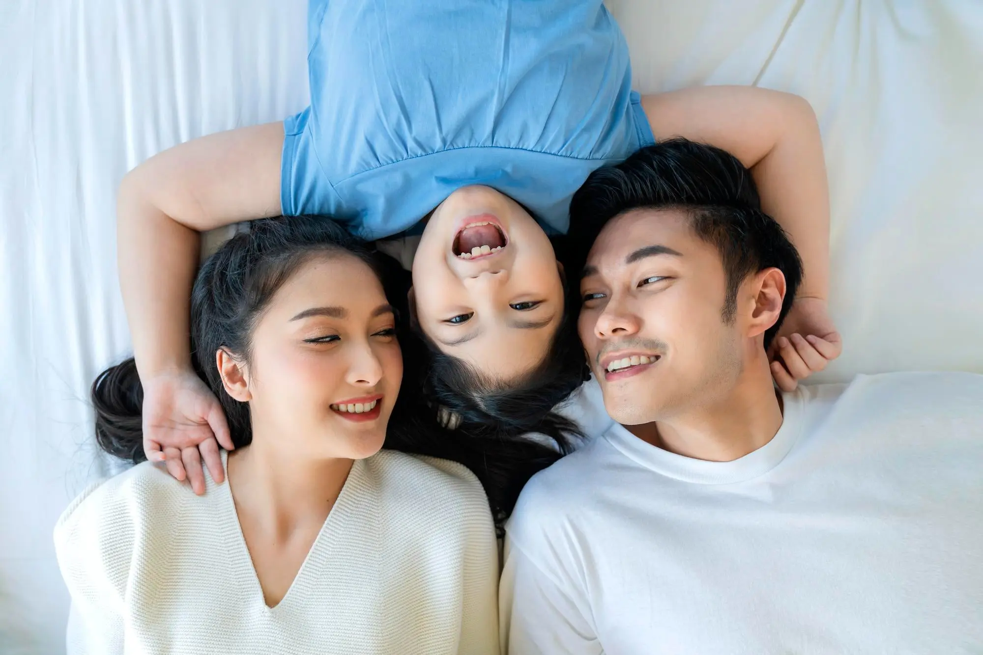 Smiling faces of two adults and a child represent best orthodontic appliances at Forsyth Pediatric Dentistry and Orthodontics in Cumming, GA, heads together on bed.