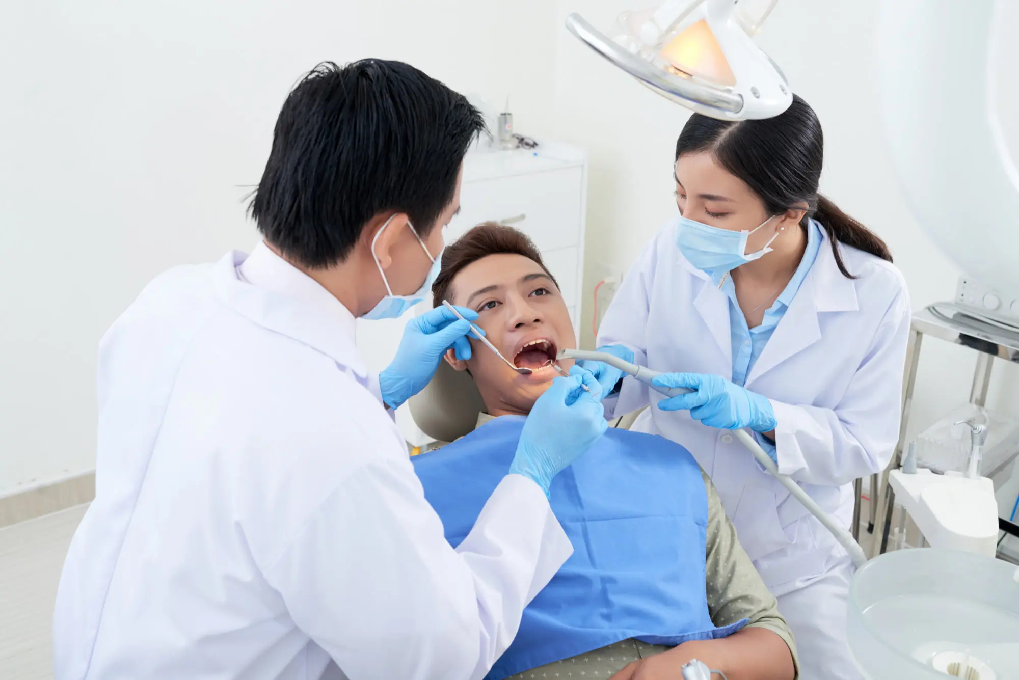 At Forsyth Pediatric Dentistry and Orthodontics in Cumming, GA, a dentist and assistant examine a patient for overbite treatment, all masked and gloved.