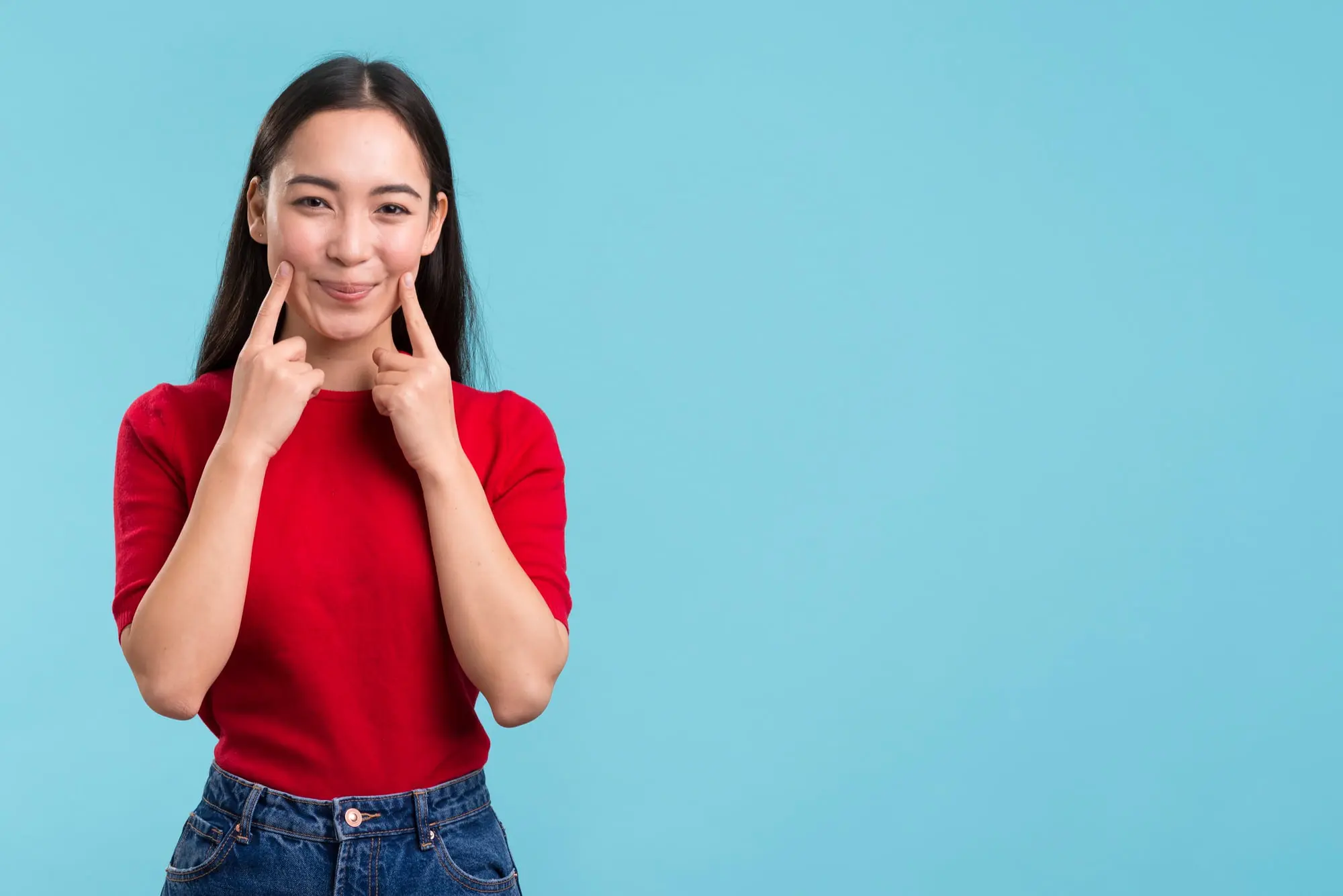 Smiling, a woman in red and blue points to her cheeks before overbite treatment at Forsyth Pediatric Dentistry and Orthodontics in Cumming, GA.