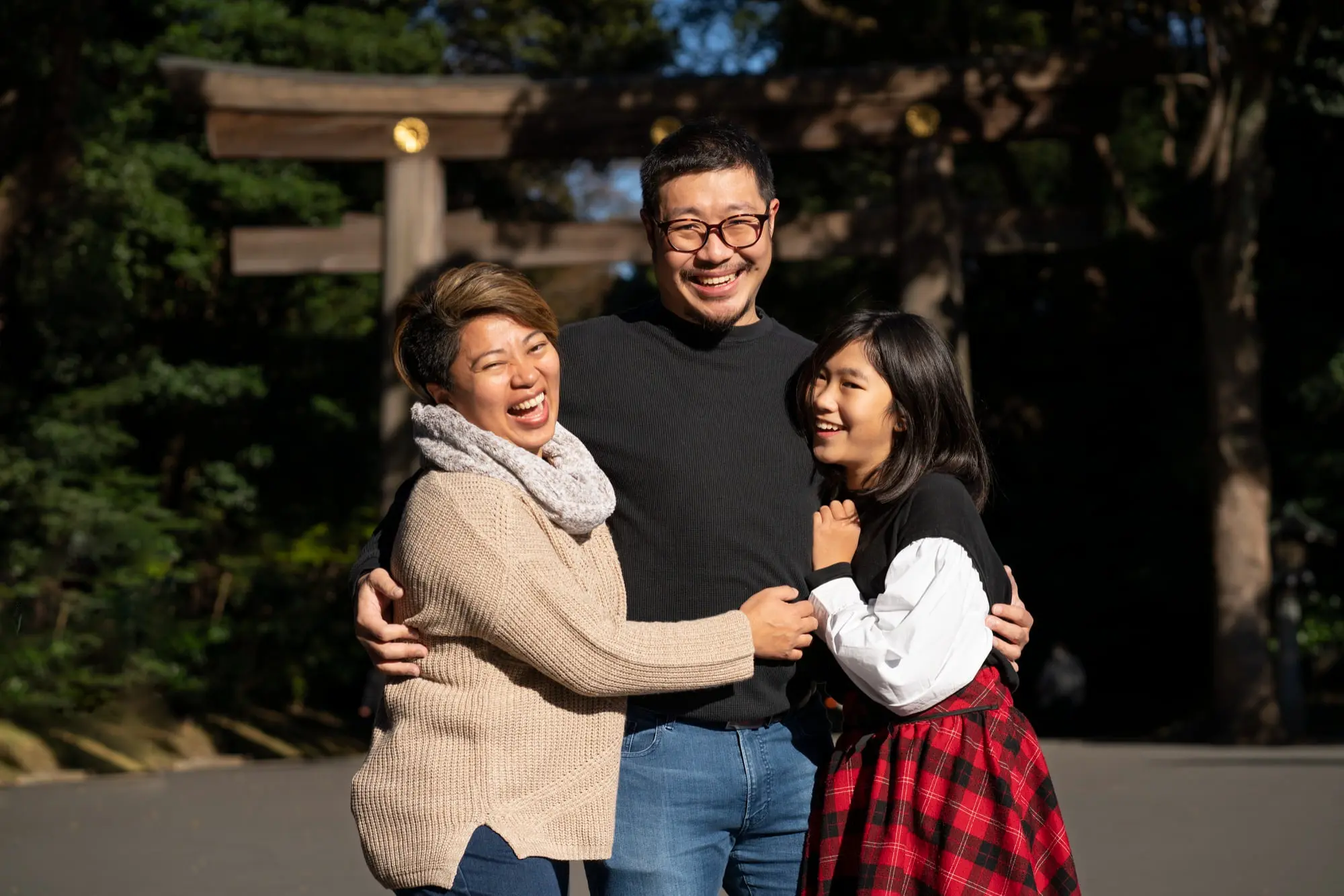 Smiling trio hug outdoors near trees and a torii gate show result underbite treatment from Forsyth Pediatric Dentistry and Orthodontics in Cumming, GA.