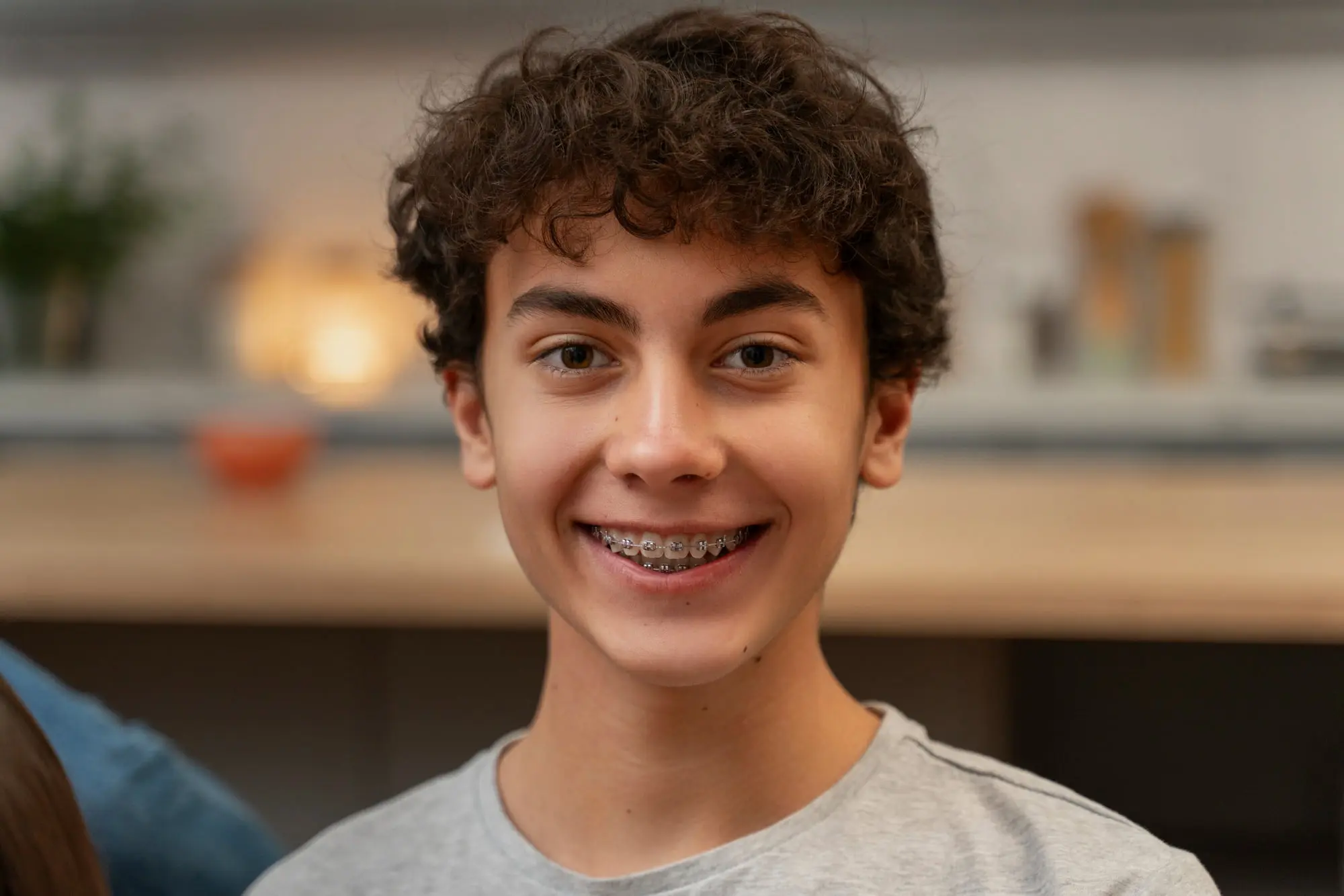 Smiling teenage boy with brown curls and metal braces at Pediatric Dentistry and Orthodontics of Forsyth - Cumming in Cumming, GA, indoors.