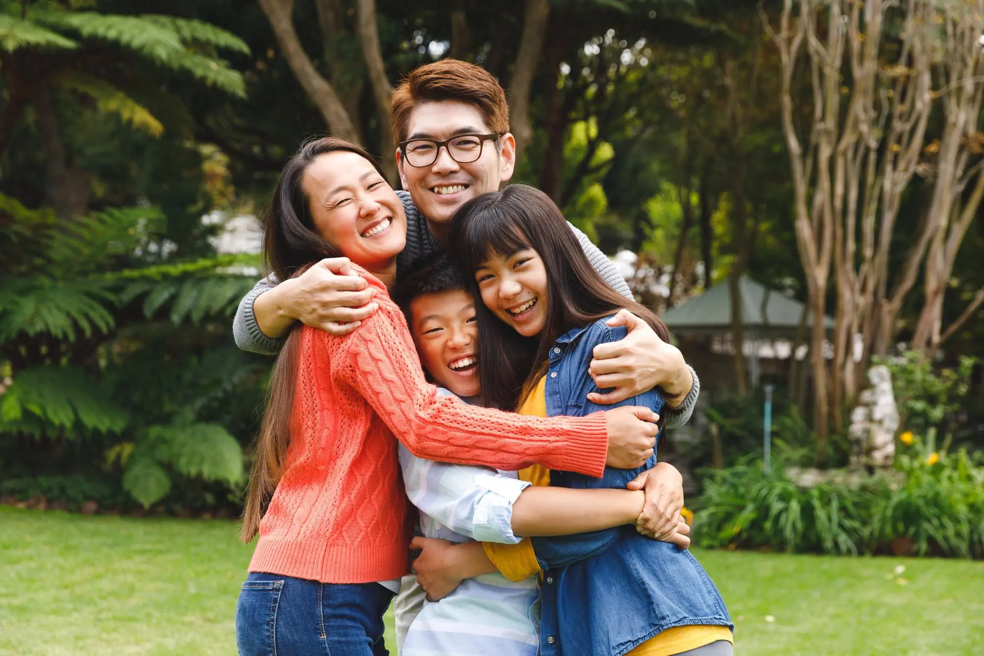 Smiling in a group hug, four people stand in a garden after overbite treatment at Forsyth Pediatric Dentistry and Orthodontics in Cumming, GA.