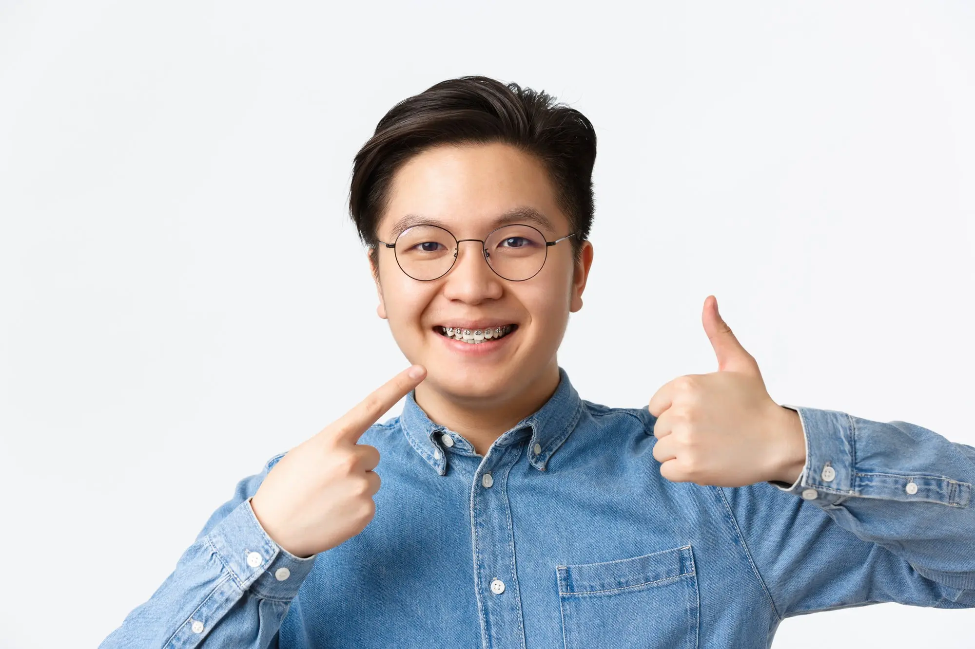 Smiling young person in glasses points to braces and gives thumbs up after visiting Pediatric Dentistry and Orthodontics of Forsyth - Cumming in Cumming, GA.