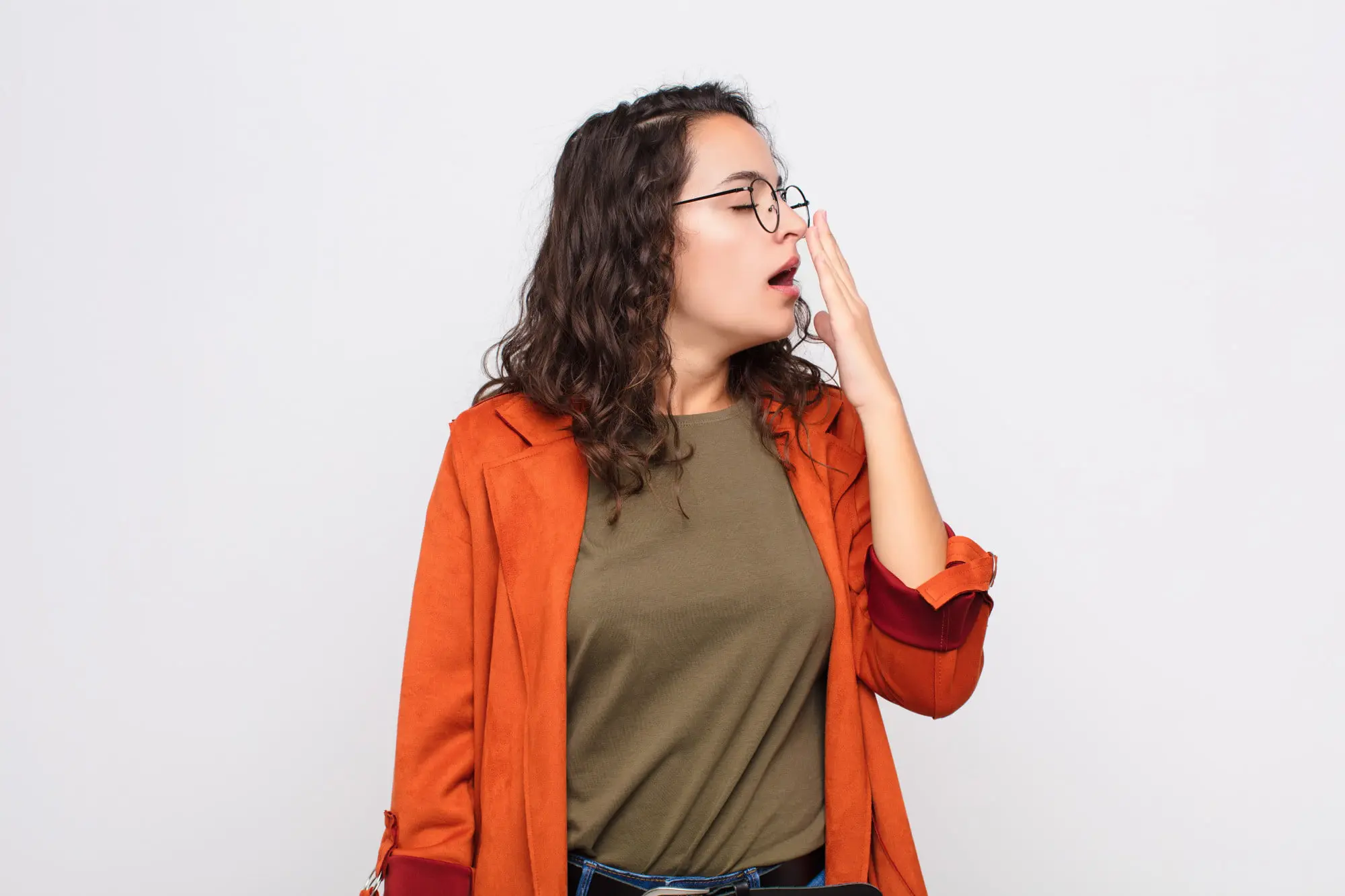 At Forsyth Pediatric Dentistry and Orthodontics in Cumming, GA, a woman with brown hair yawns, wearing glasses and an orange jacket like have mouth breathing issue and underbite.