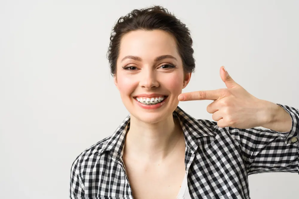A young woman in a checkered shirt points to her metal braces, representing Pediatric Dentistry and Orthodontics of Forsyth - Cumming in Cumming, GA.