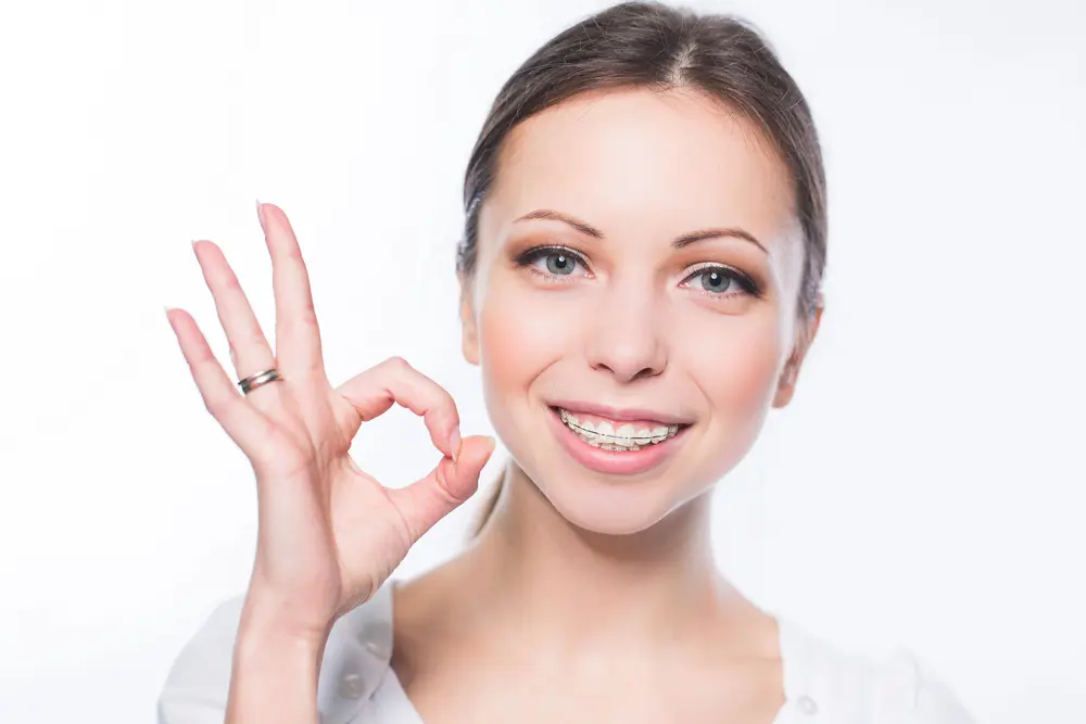 Smiling young woman with clear braces makes an "OK" gesture, promoting Pediatric Dentistry and Orthodontics of Forsyth - Cumming in Cumming, GA.