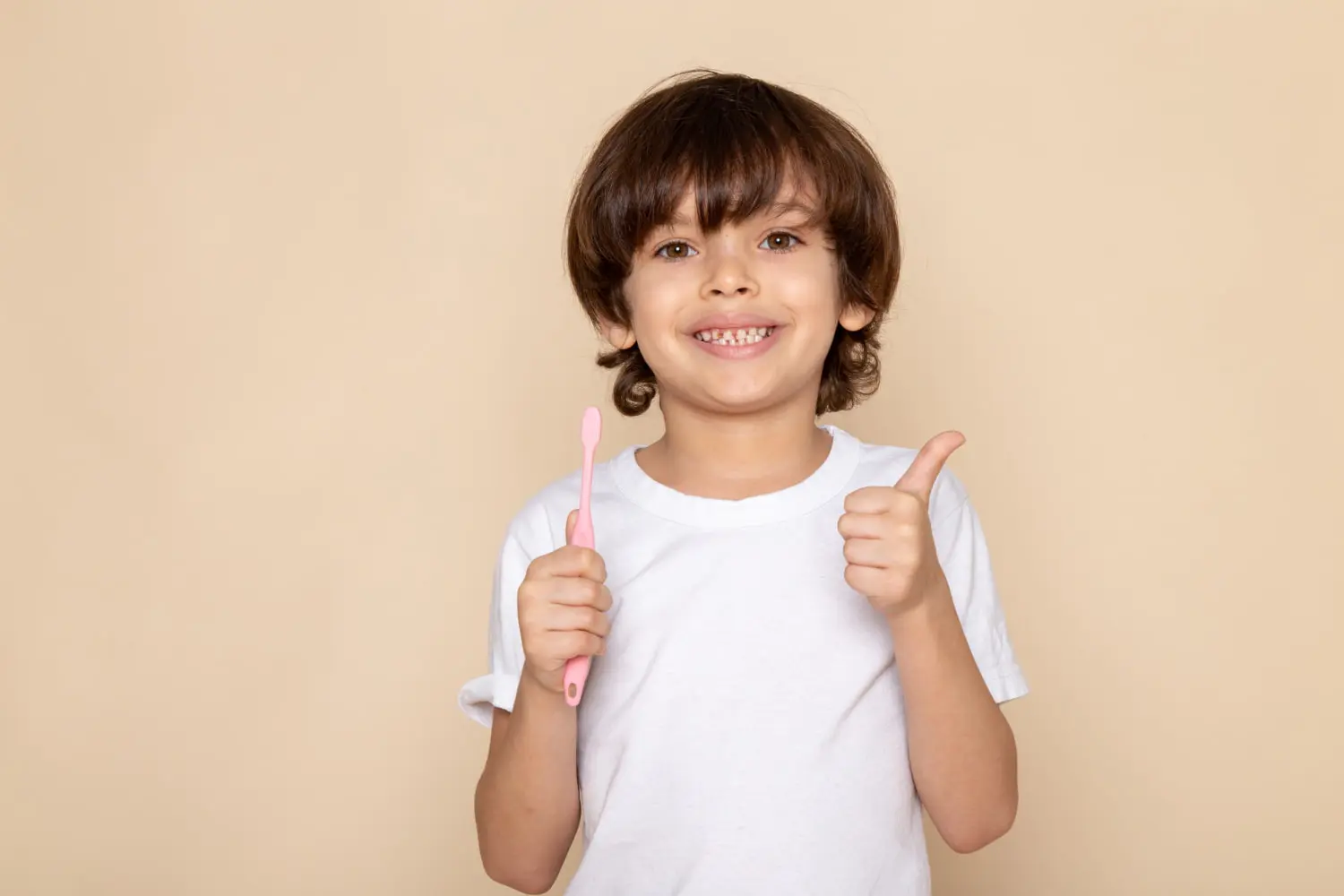 Child in white t-shirt with pink toothbrush and thumbs up, showing that Forsyth Pediatric Dentistry and Orthodontics in Cumming, GA helps families manage orthodontic costs.