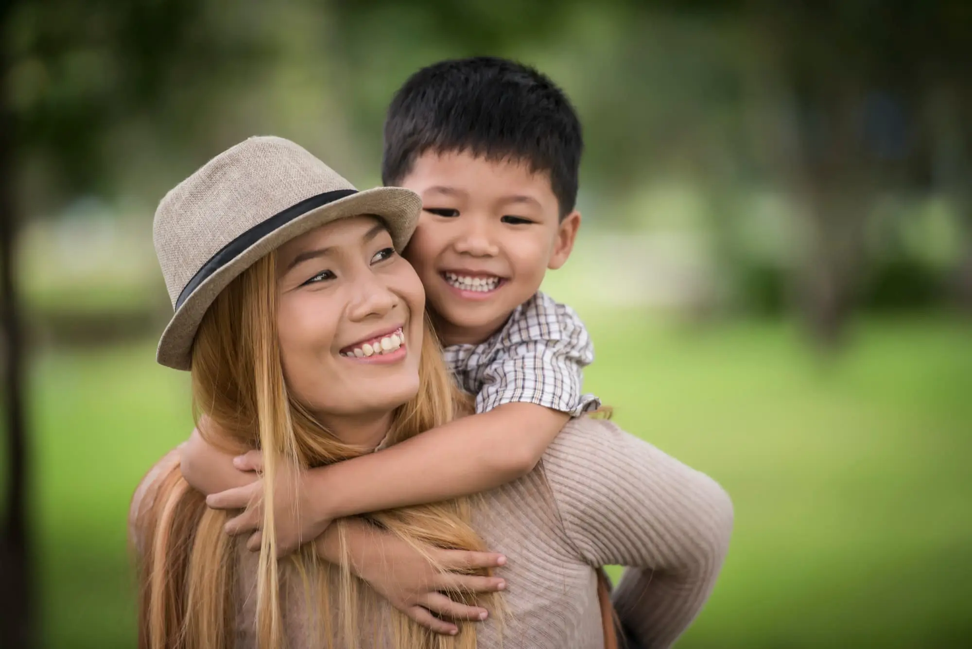 A woman in a hat smiles as a boy hugs her outdoors, showing the joy Forsyth Pediatric Dentistry and Orthodontics in Cumming, GA brings.