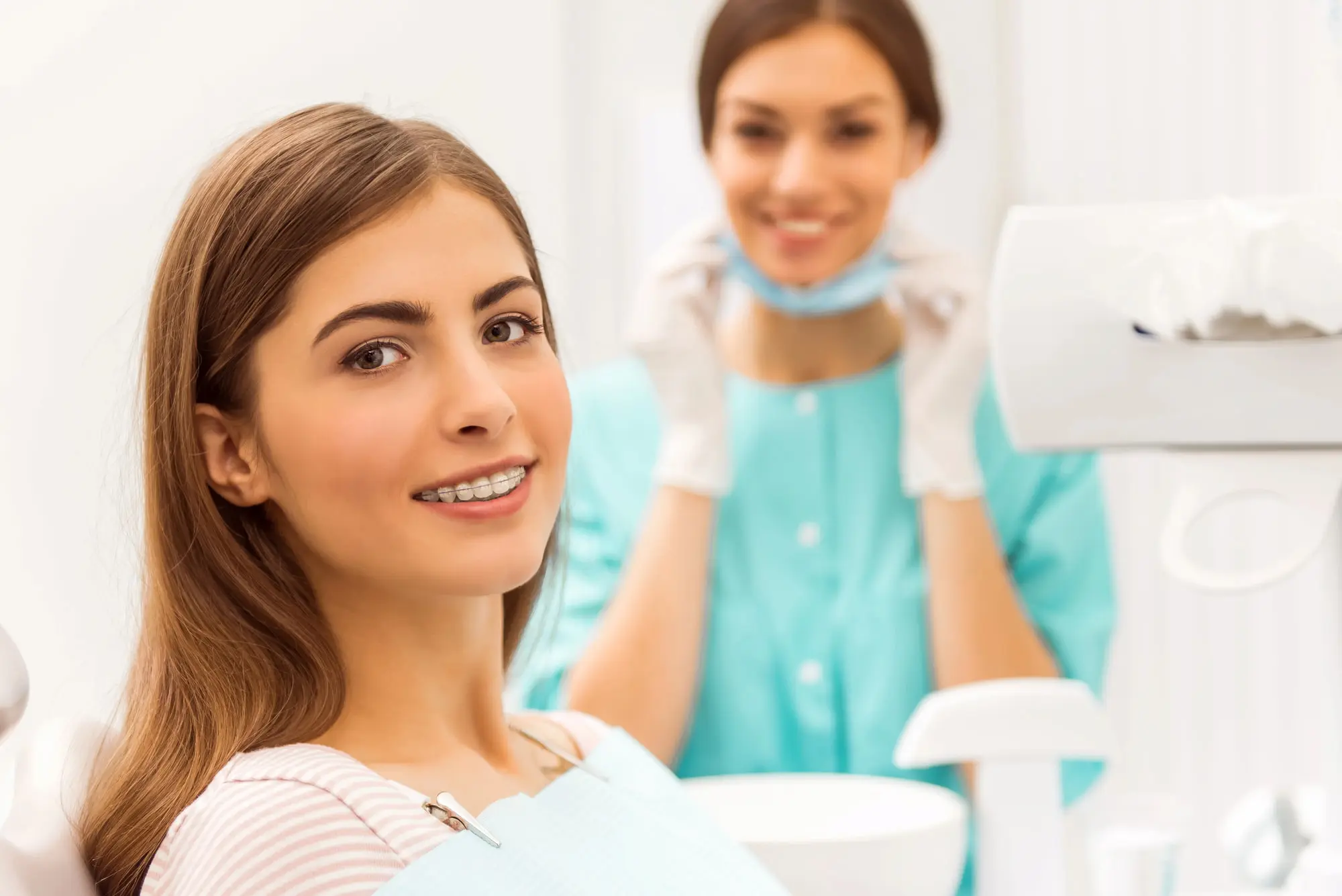 A teen with braces smiles in a dental chair at Forsyth Pediatric Dentistry and Orthodontics in Cumming, GA, dentist behind her after jaw surgery.