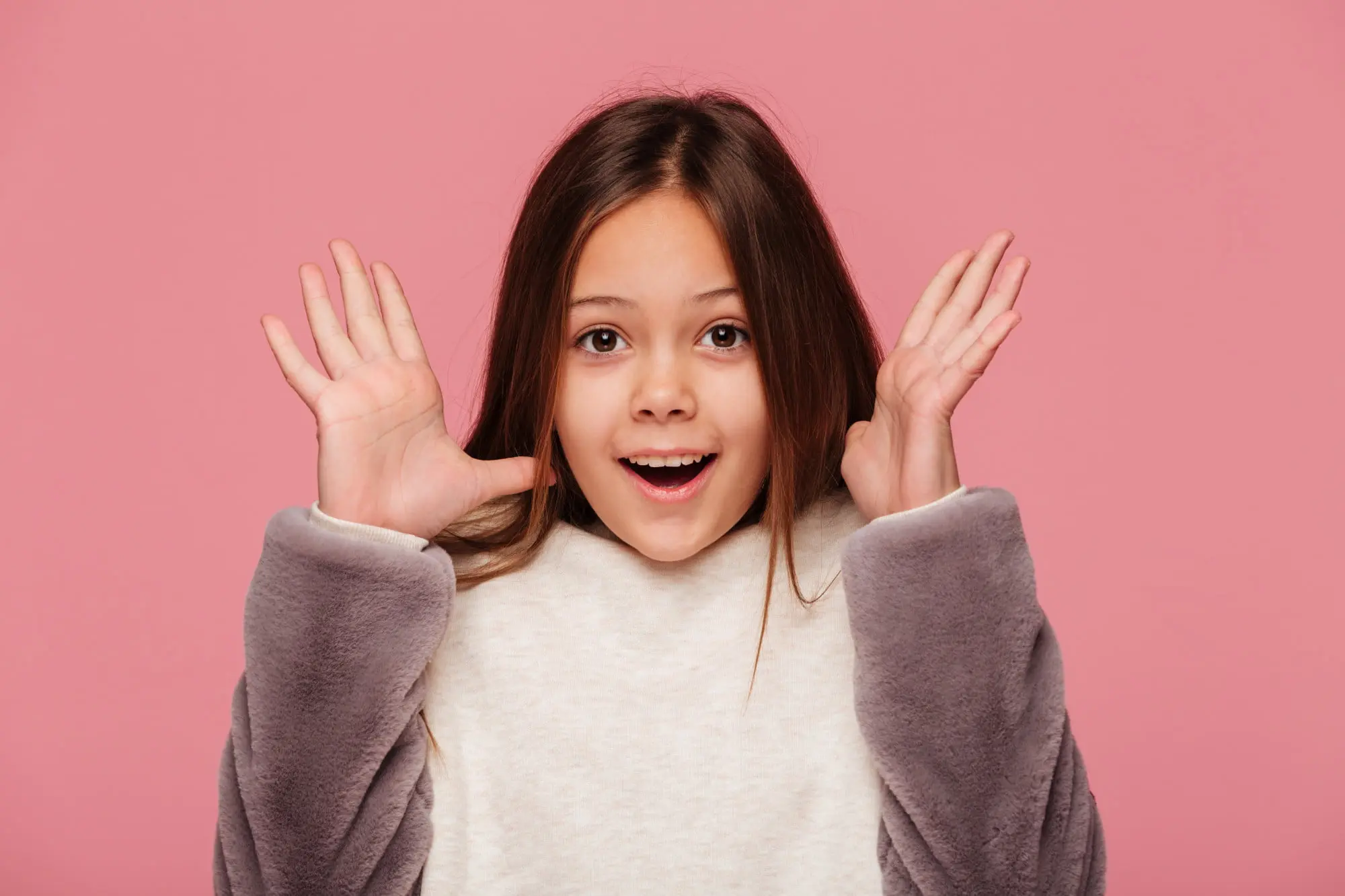 A surprised young girl poses in front of a pink background, promoting early orthodontics at Forsyth Pediatric Dentistry and Orthodontics in Cumming, GA.