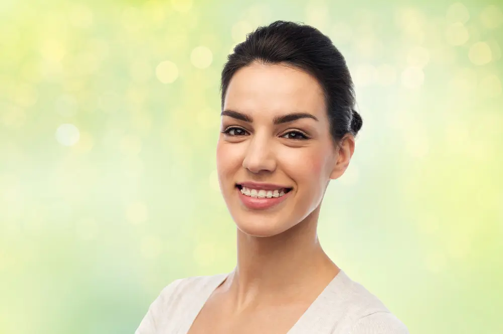 Smiling woman with dark hair and clear braces at Forsyth Pediatric Dentistry and Orthodontics in Cumming GA, outdoors.