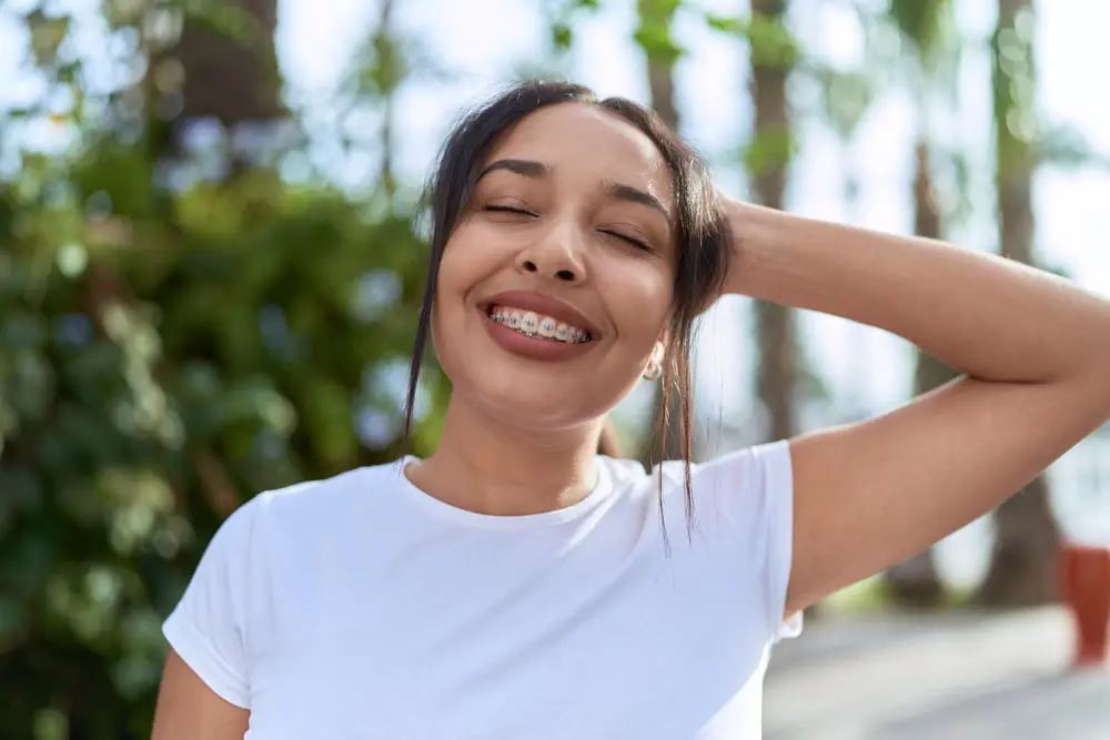 Smiling young woman with adult braces represents Forsyth Pediatric Dentistry and Orthodontics in Cumming, GA outdoors in greenery.