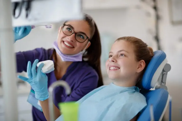 At Forsyth Pediatric Dentistry and Orthodontics in Cumming, GA, a dentist shows a dental model to a smiling young girl - Fluoride Safety for Children in Cumming, GA