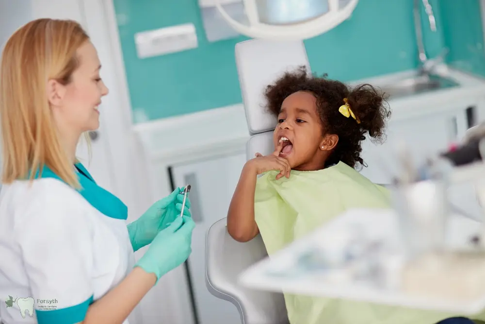 At Forsyth Pediatric Dentistry and Orthodontics in Cumming, GA, a dentist explains dental sealants to a young girl in the chair.