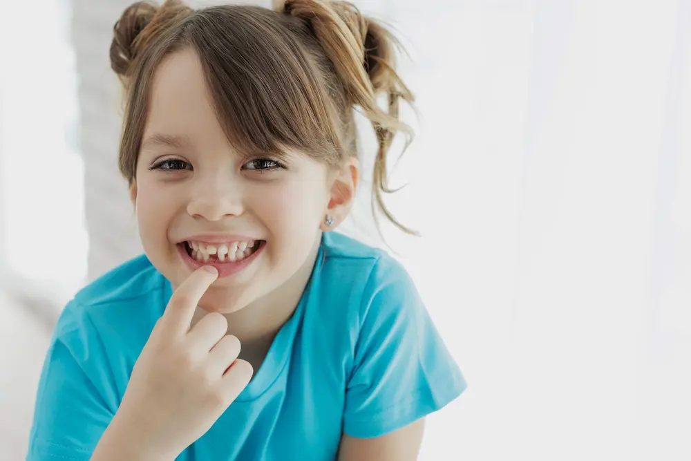 A smiling girl in pigtails shows her missing tooth, reflecting moments Forsyth Pediatric Dentistry and Orthodontics in Cumming, GA helps treat.