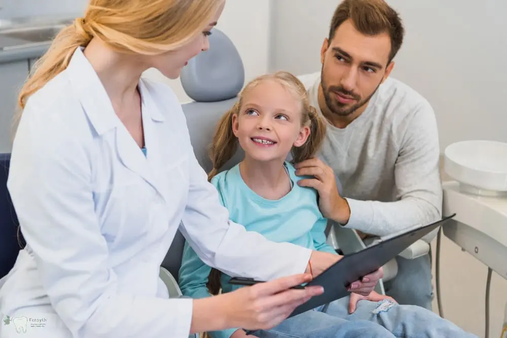 A dentist at Forsyth Pediatric Dentistry and Orthodontics in Cumming, GA, discusses toothbrush choices by age with a girl and her dad - Best Toothbrush for Kids by Age – Cumming Parent Guide