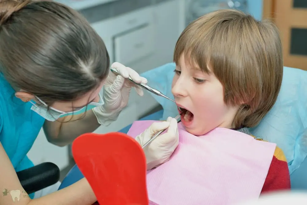 A child with a pink bib gets a dental exam by a gloved dentist at Forsyth Pediatric Dentistry and Orthodontics in Cumming, GA - School Dental Health Programs in Cumming, GA 