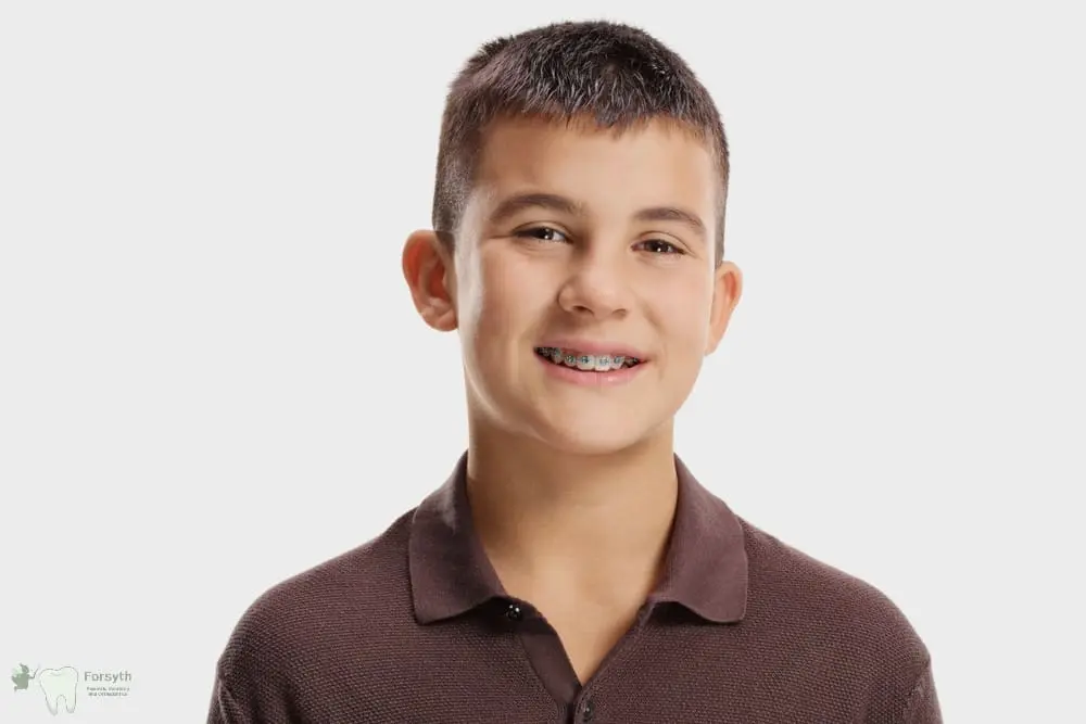 Boy with short dark hair, brown polo, and metal braces smiles at Forsyth Pediatric Dentistry and Orthodontics in Cumming, GA - Braces for Teens in Cumming: What Parents Should Know 