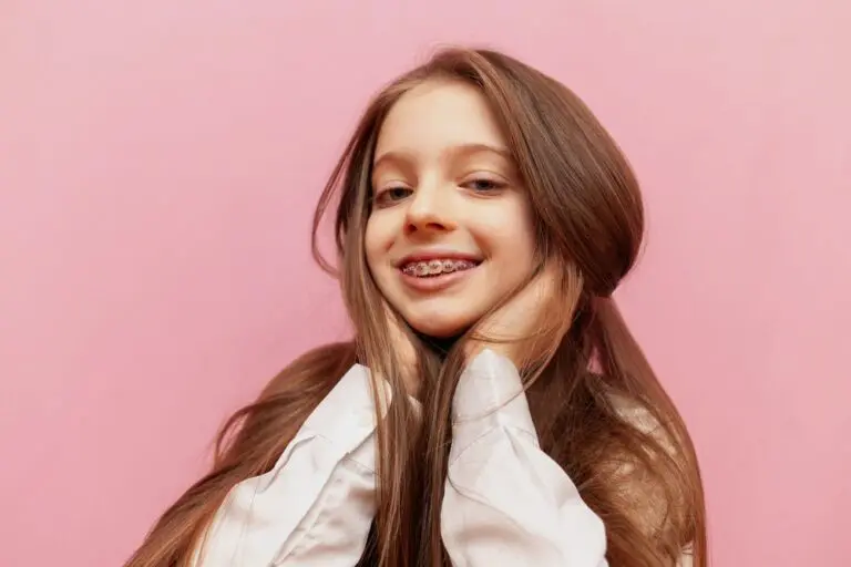 A smiling girl with long brown hair and teen braces poses against a pink background at Forsyth Pediatric Dentistry and Orthodontics in Cumming, GA - Braces for Teens in Cumming: What Parents Should Know
