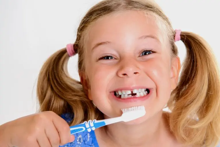 Young girl with missing teeth and pink hair ties holding toothbrush, at Forsyth Pediatric Dentistry and Orthodontics in Cumming, GA - How to Prevent Baby Bottle Decay in Cumming, GA