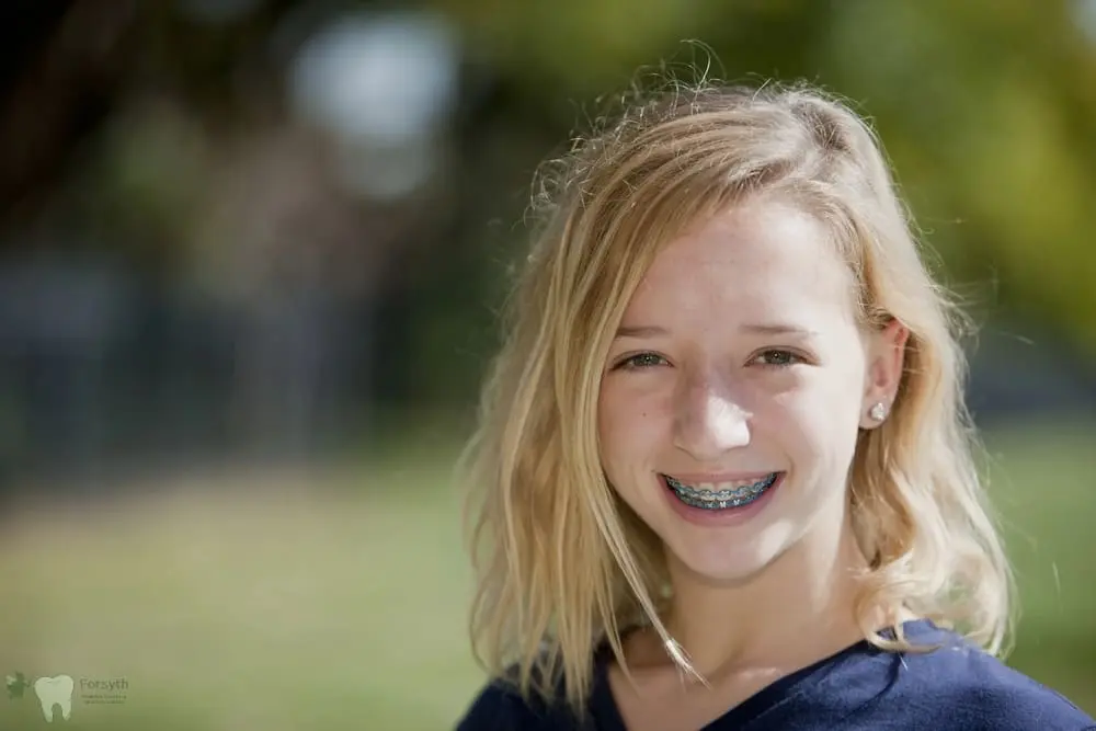 A smiling blonde girl with braces, at Forsyth Pediatric Dentistry and Orthodontics in Cumming, GA, stands outdoors - Tooth-Friendly Snacks for Kids: Dentist Recommendations from Cumming, GA